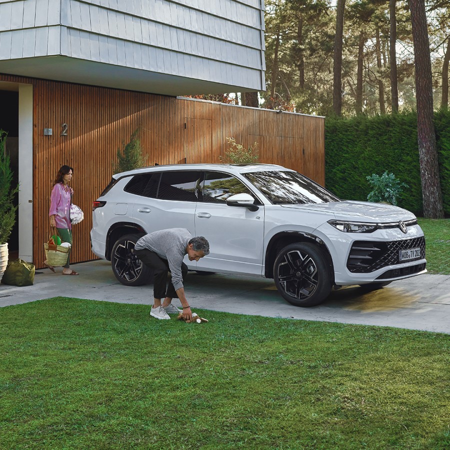 Der VW Tayron vor einem Haus mit 2 Personen